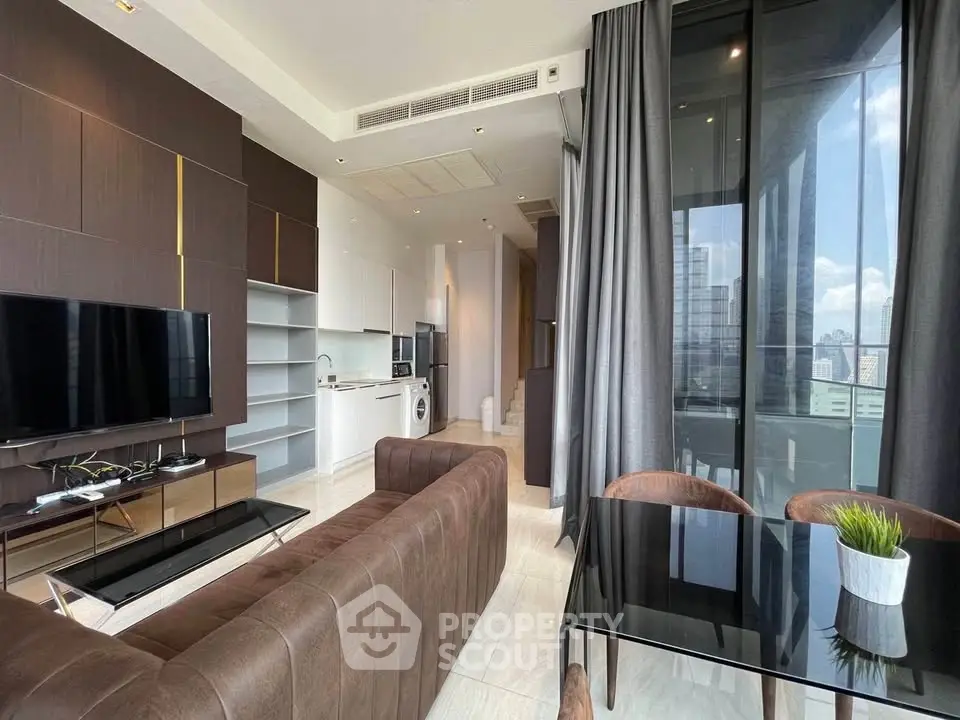 Modern living room with open kitchen and city view, featuring sleek furniture and floor-to-ceiling windows.