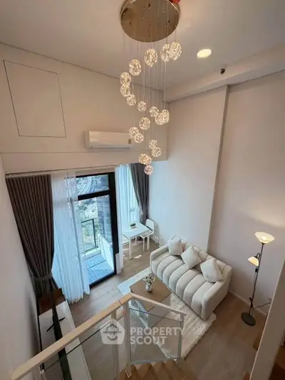 Modern loft-style living room with elegant chandelier and cozy seating area, featuring floor-to-ceiling windows.