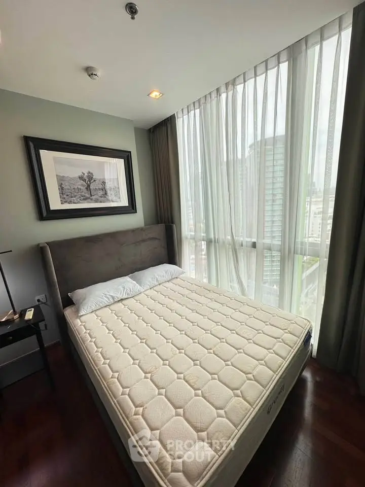 Modern bedroom with large windows and city view, featuring a comfortable bed and stylish decor.