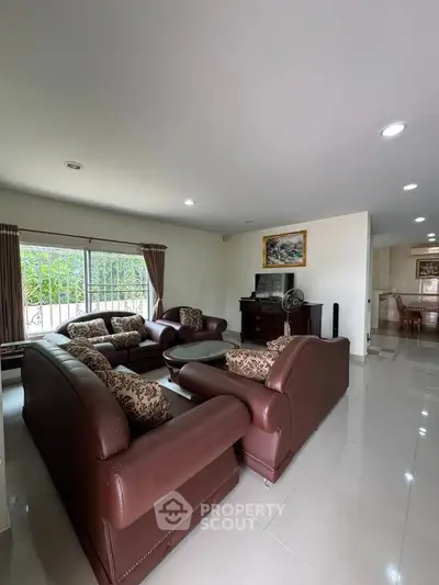 Spacious living room with elegant brown leather sofas and large window view.