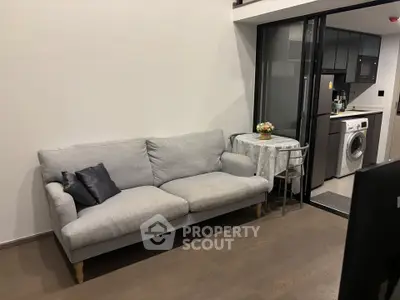 Modern living room with cozy sofa and open kitchen featuring washing machine and sleek appliances.