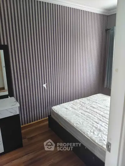 Cozy bedroom with striped wallpaper and wooden flooring, featuring a bed and a dresser with mirror.