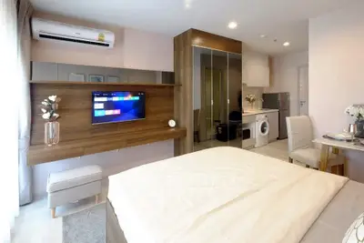 Modern studio apartment with sleek design, featuring a wall-mounted TV, mirrored wardrobe, and in-unit washer.