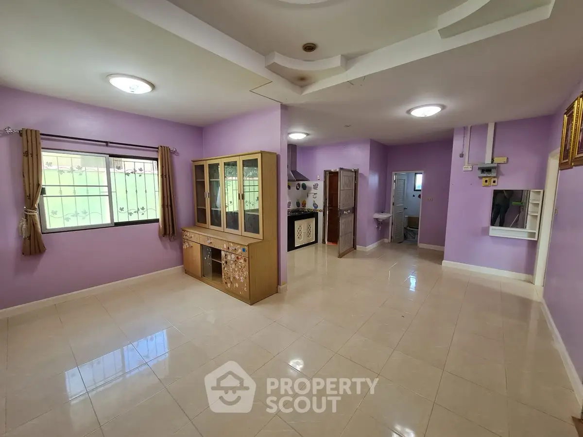 Spacious living area with glossy tiled flooring, lavender walls, and ample natural light streaming through multiple windows, perfect for family gatherings.