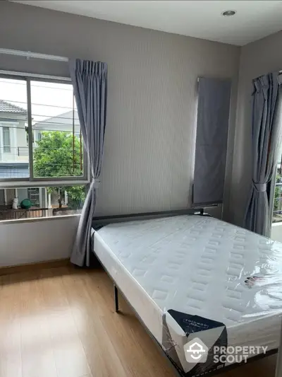 Spacious bedroom with large windows draped in elegant curtains, offering ample natural light and a serene neighborhood view, featuring pristine wooden flooring.