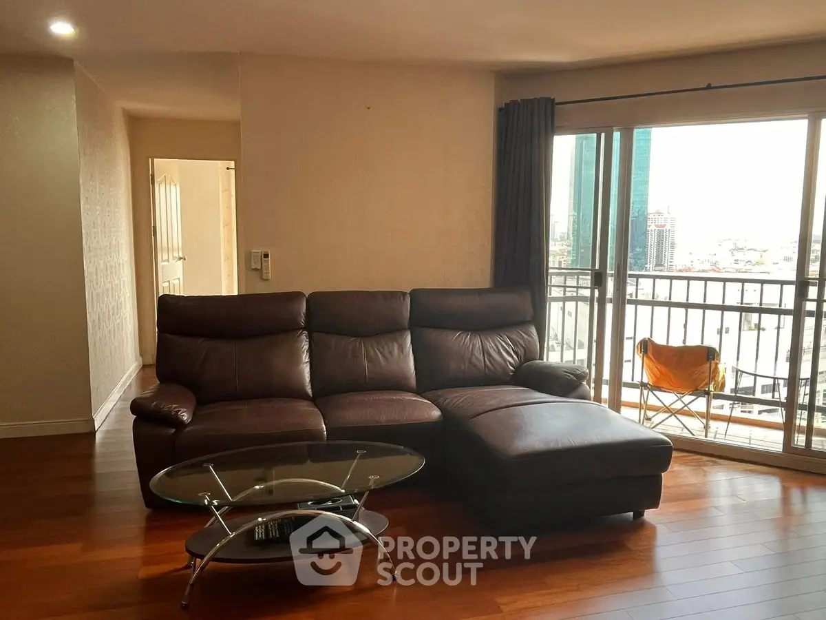Spacious living room with leather sofa and city view balcony.