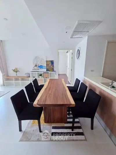 Modern dining area with sleek wooden table and black chairs in a stylish open-plan living space.
