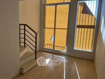 Bright living room with large windows and staircase, featuring modern design and natural light.