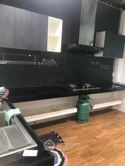Modern kitchen with sleek black cabinets and gas stove, featuring wooden flooring and open shelving.