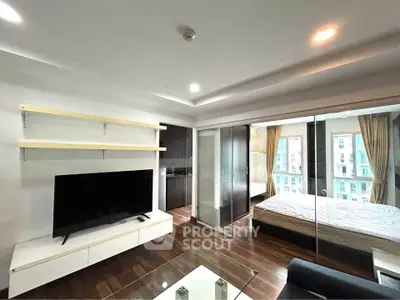 Modern living room with glass partition to bedroom, featuring sleek TV unit and wooden flooring.