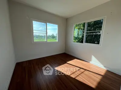Bright empty room with wooden flooring and large windows offering scenic views.