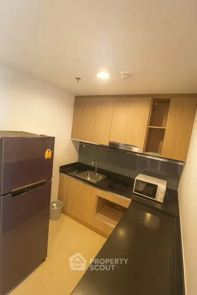 Modern kitchen with sleek black countertops, wooden cabinets, and stainless steel appliances.