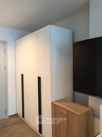 Modern bedroom with sleek wardrobe and mounted TV, showcasing minimalist design and functionality.