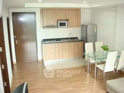 Modern kitchen with wooden cabinets, stainless steel appliances, and a glass dining table in a cozy apartment.