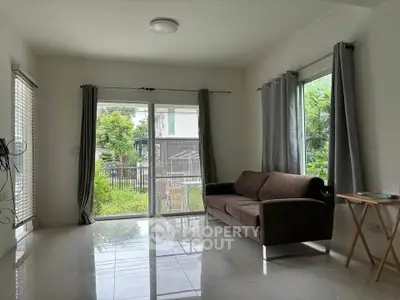 Bright living room with large windows and garden view, featuring a modern brown sofa and sleek tiled flooring.