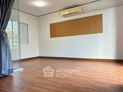 Spacious empty room with wooden flooring and large window, perfect for customization.