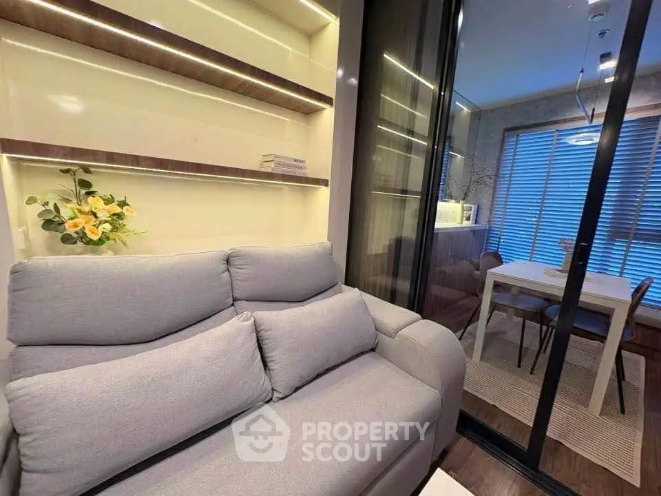 Modern living room with cozy gray sofa and elegant dining area separated by glass doors.