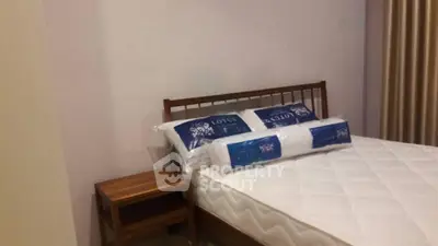 Cozy bedroom with wooden bed frame and side table, featuring plush pillows and a comfortable mattress.
