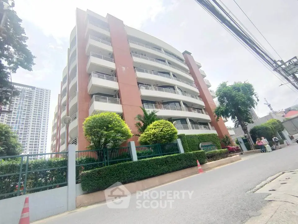 Modern multi-story residential building with lush greenery and secure fencing in urban setting.