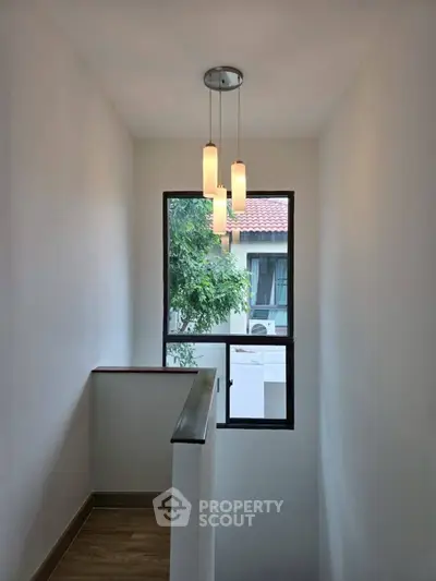 Bright stairwell with modern lighting and window view of neighboring house.