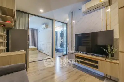 Modern living room with wooden flooring, large TV, and sliding glass doors leading to a bedroom.