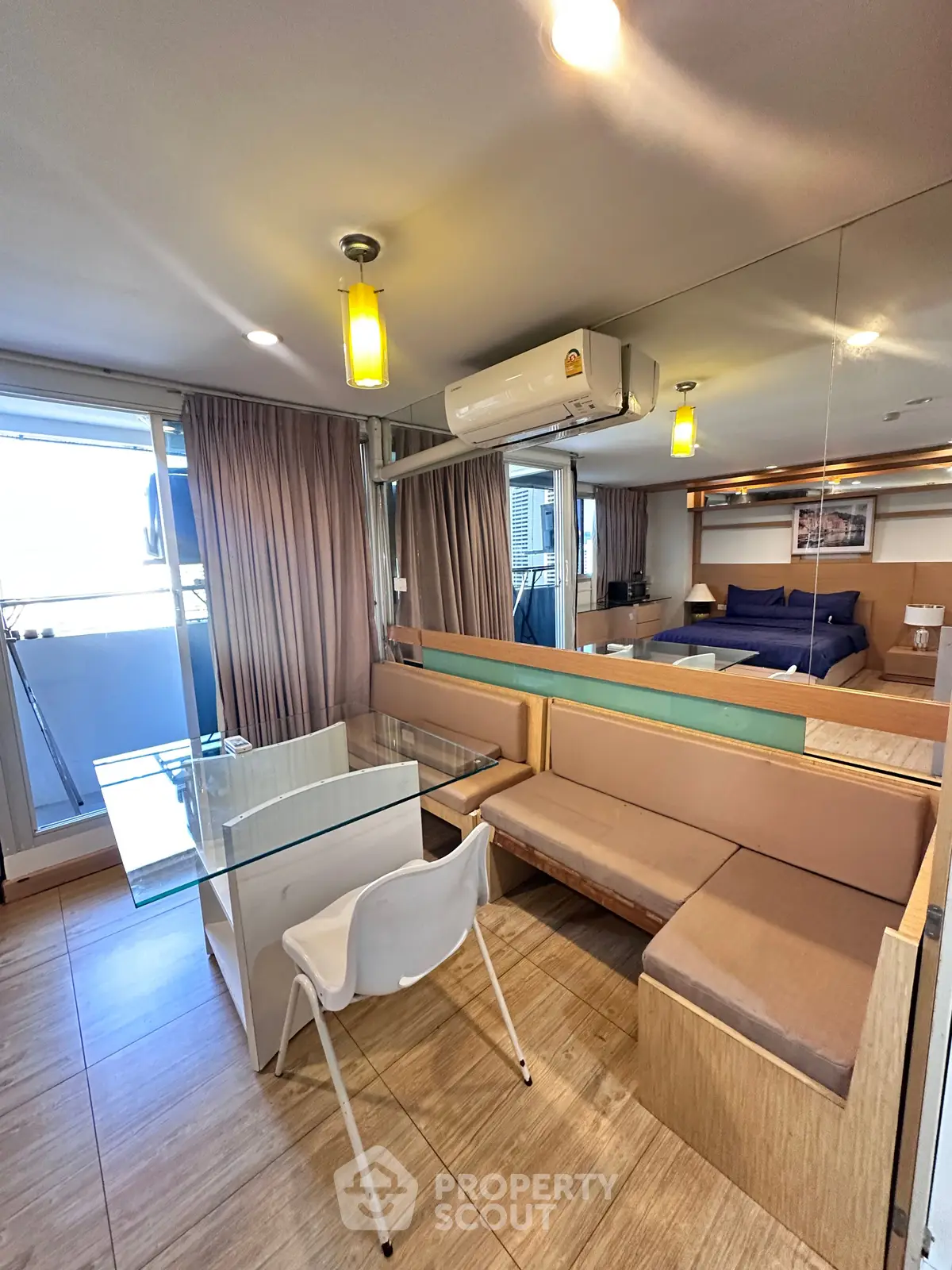 Modern studio apartment with glass dining table and cozy seating area, featuring air conditioning and stylish lighting.