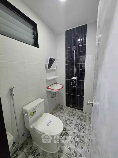 Modern bathroom with sleek black and white tiles, featuring a shower and toilet.