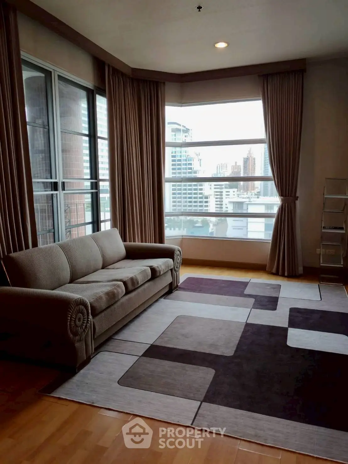 Spacious living room with large windows offering stunning city views, featuring elegant curtains and a cozy sofa.