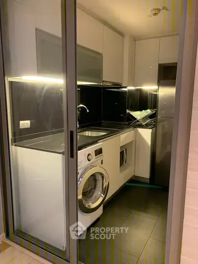 Modern compact kitchen with sleek appliances and washing machine in a stylish apartment.