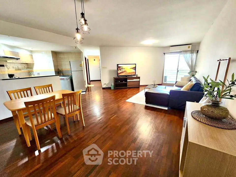 Spacious open-plan living room with wooden flooring and modern furnishings in a bright apartment.