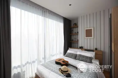 Cozy bedroom with guitar and hat on bed, large window with sheer curtains, modern decor.