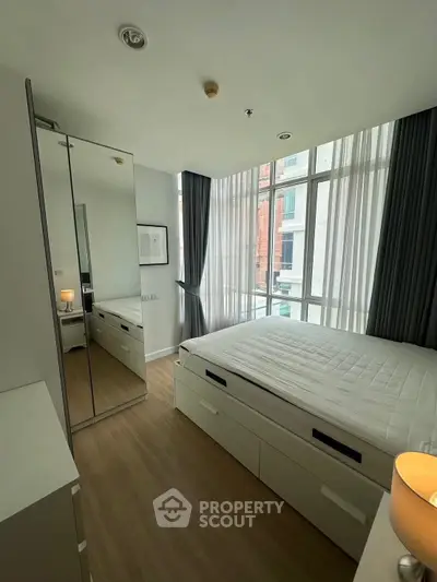 Modern bedroom with large windows and sleek furniture in a high-rise apartment.