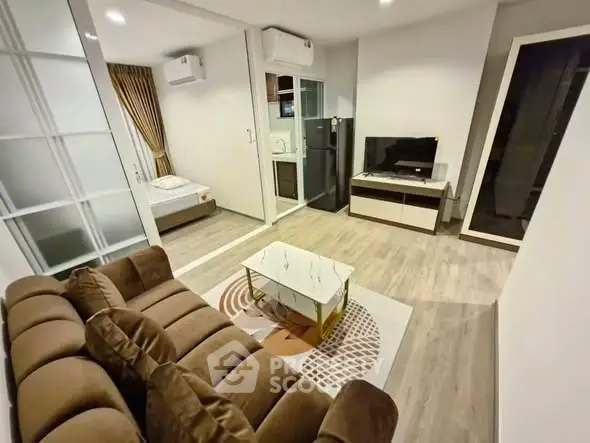 Modern living room with cozy brown sofa, sleek TV unit, and view into a compact bedroom.