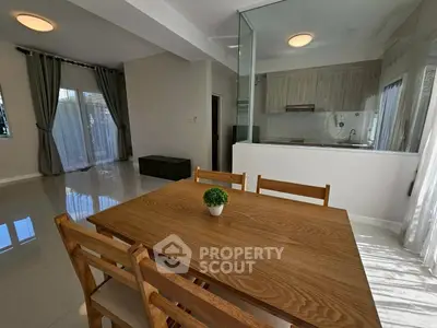 Modern dining area with wooden table and chairs, adjacent to sleek kitchen.