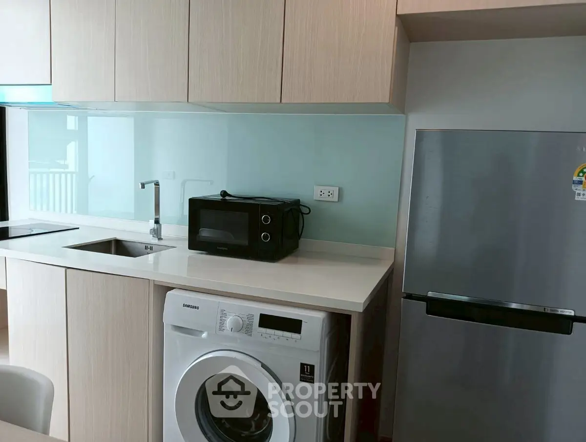 Modern kitchen with sleek appliances including washing machine and fridge, ideal for urban living.