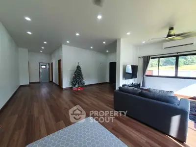 Spacious living room with modern decor and Christmas tree, featuring large windows and wooden flooring.