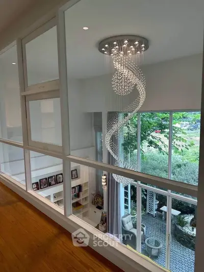 Elegant modern living room with stunning chandelier and large windows overlooking lush greenery.