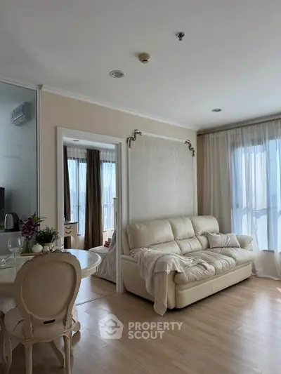 Elegant living room with cream sofa and dining area, featuring large windows and stylish decor.