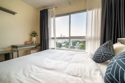 Sunlit bedroom with expansive windows offering a serene view, complemented by modern furnishings and a cozy ambiance.