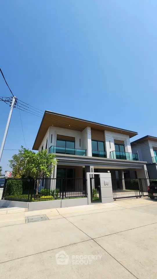 Modern two-story house with large windows and balcony in a serene neighborhood.