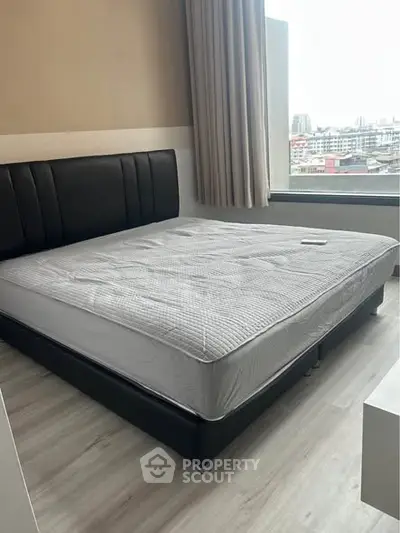 Modern bedroom with large window offering city view and stylish bed frame.