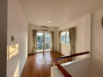 Spacious living room with large windows and balcony access, featuring elegant wooden flooring and abundant natural light.