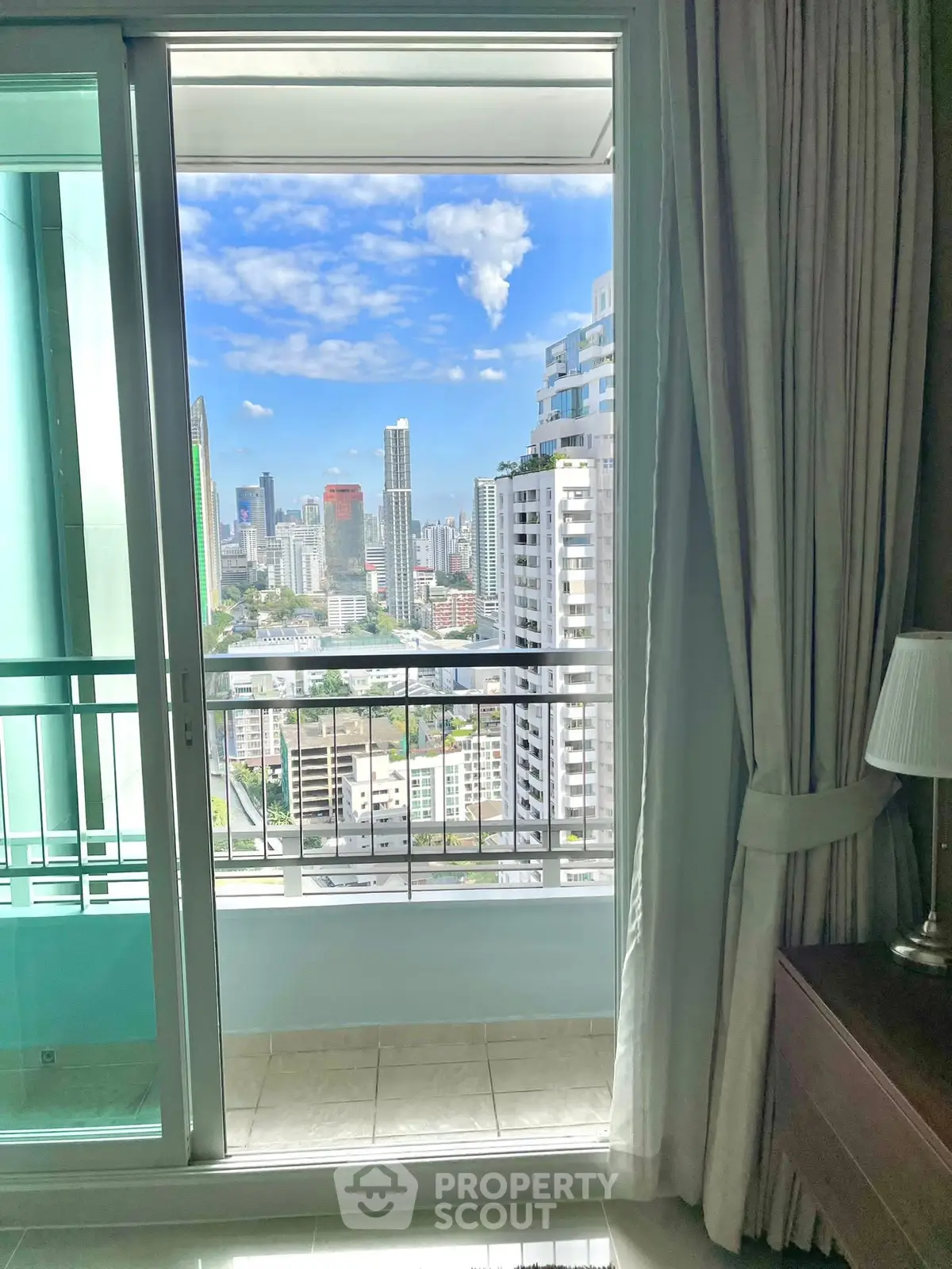 Stunning city view from a high-rise balcony with elegant interior curtains.