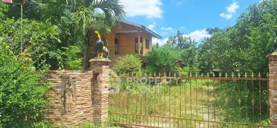 Charming rustic house with lush garden and gated entrance under clear blue sky.