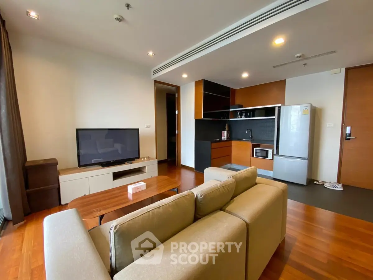 Modern living room with open kitchen, featuring sleek appliances and cozy seating area.
