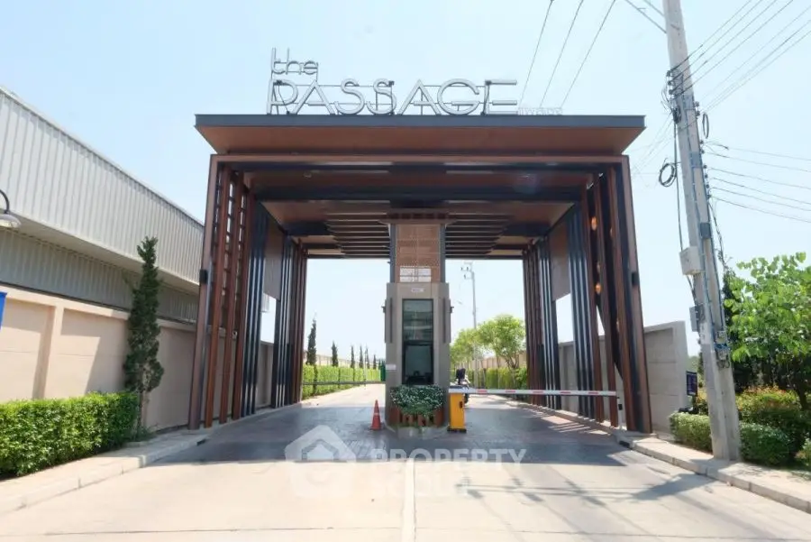 Modern gated entrance of luxury residential complex with sleek design and lush greenery.