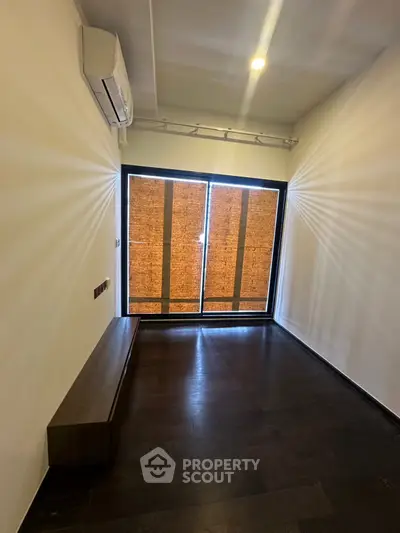 Minimalist room with dark flooring and large window, featuring air conditioning.