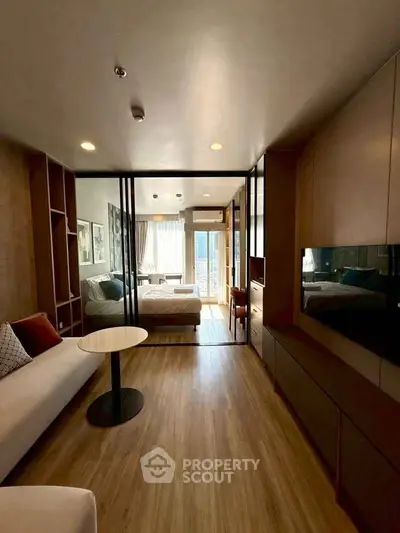 Modern living room with open layout and natural light, featuring stylish furniture and a view into the bedroom.