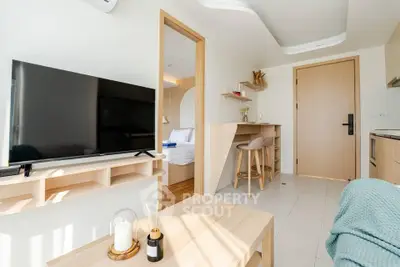 Modern living room with TV, stylish furniture, and open view into bedroom