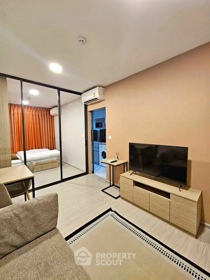 Modern living room with TV, sofa, and view into bedroom and kitchen with washing machine.